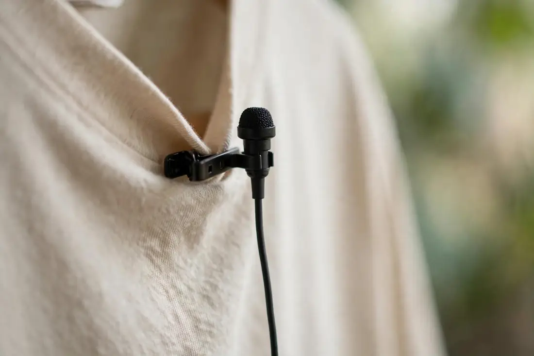 Close-up of a small wired lavalier microphone clipped to a shirt collar
