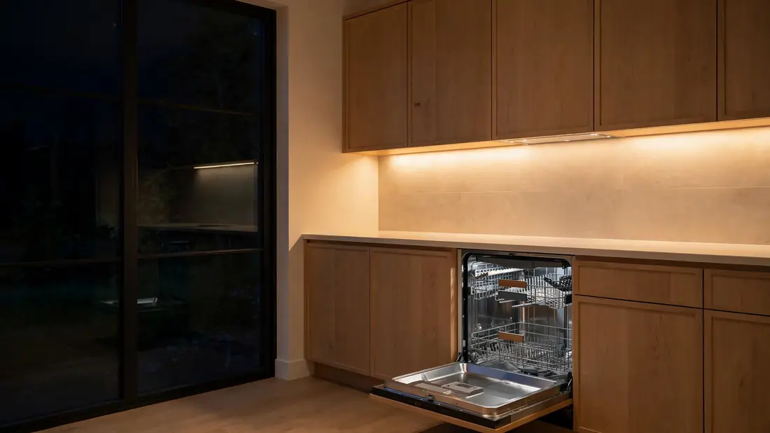Warm-lit kitchen at night with a cleared counter and open dishwasher