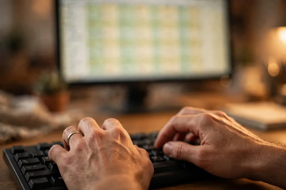 Close-up of hands on a keyboard with a blurred spreadsheet on a monitor